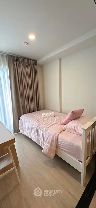 Cozy bedroom with soft pink bedding and natural light, perfect for relaxation.