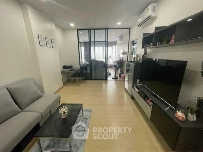 Modern living room with sleek design and glass partition, featuring a cozy sofa and large TV unit.
