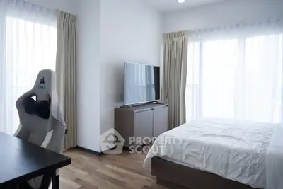 Modern bedroom with sleek furniture and natural light, featuring a stylish gaming chair and flat-screen TV.