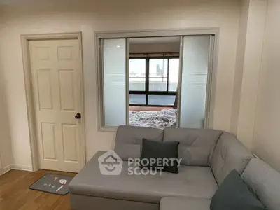 Cozy living room with modern gray sofa and view into bedroom through interior window.