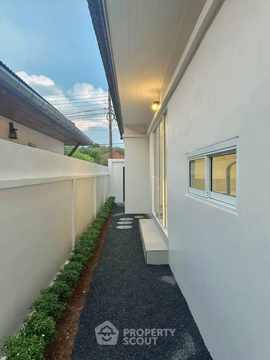 Modern exterior side pathway with clean white walls and lush greenery