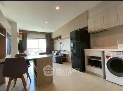 Modern open-plan living room with kitchen, featuring sleek appliances and large window view.