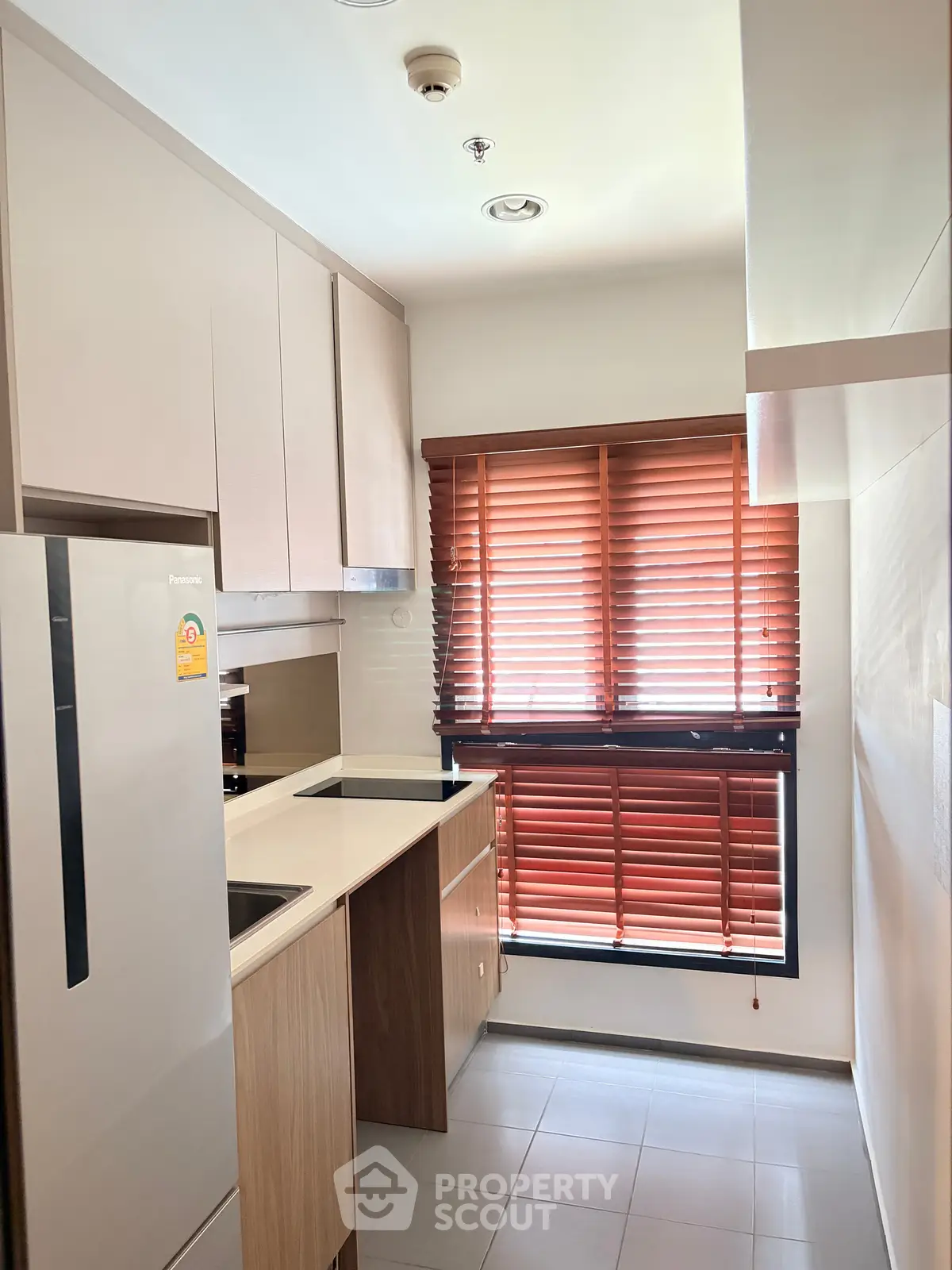 Modern kitchen with sleek cabinetry and large window blinds, featuring a built-in fridge and minimalist design.