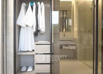 Modern bathroom with glass shower and open wardrobe showcasing robes and slippers.