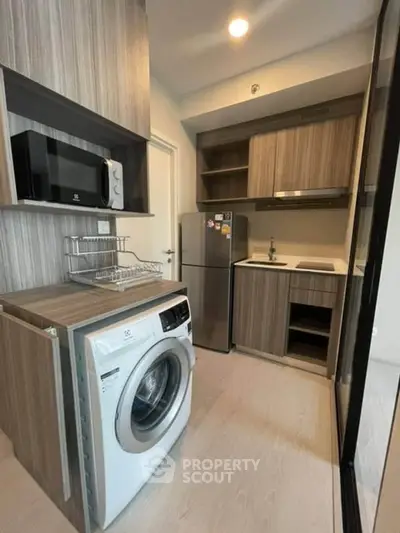 Modern compact kitchen with washing machine and microwave in stylish apartment.
