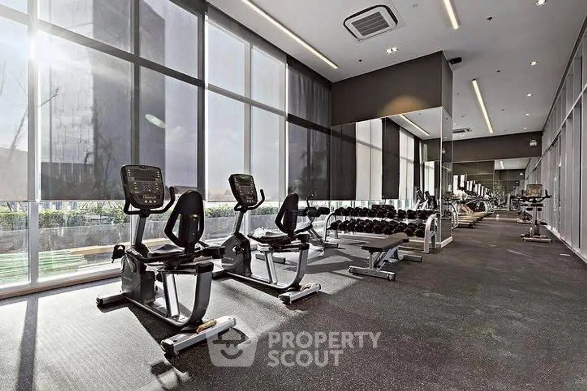 Modern gym with state-of-the-art equipment and floor-to-ceiling windows in luxury building.