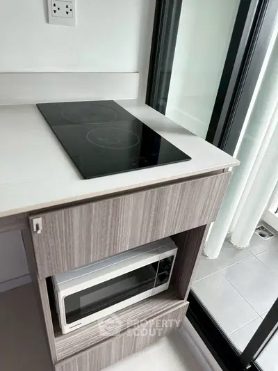 Modern kitchen with sleek induction cooktop and built-in microwave near balcony.