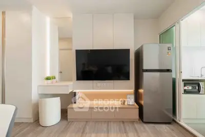 Modern living room with sleek TV setup and stainless steel fridge in stylish apartment.