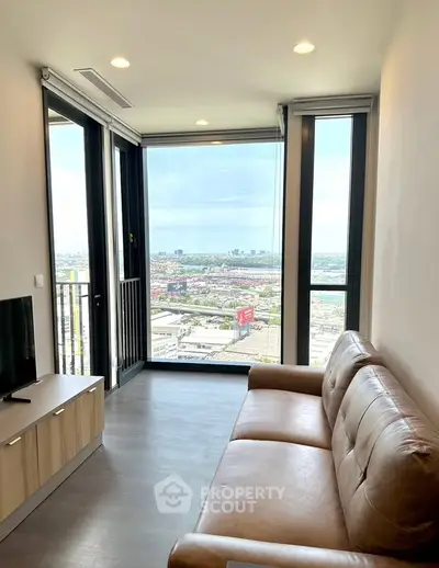 Modern living room with large windows offering stunning city views, featuring a cozy leather sofa and sleek wooden TV stand.