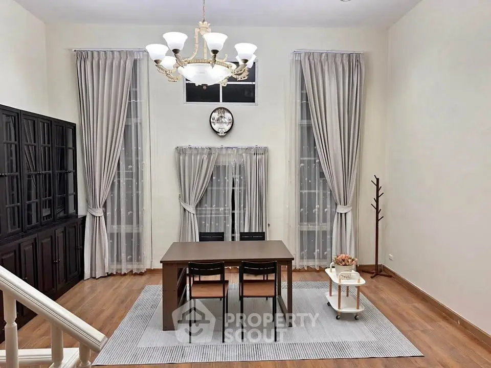 Elegant dining area with chandelier, wooden table, and floor-to-ceiling windows with curtains.