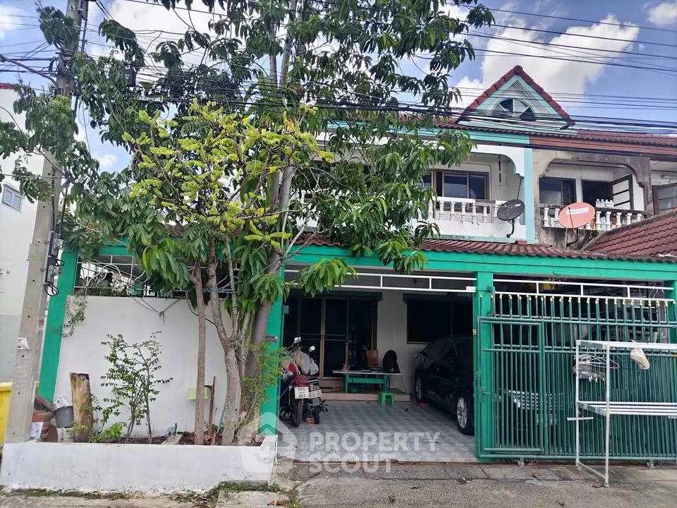 Charming two-story house with balcony and gated parking in a suburban neighborhood.