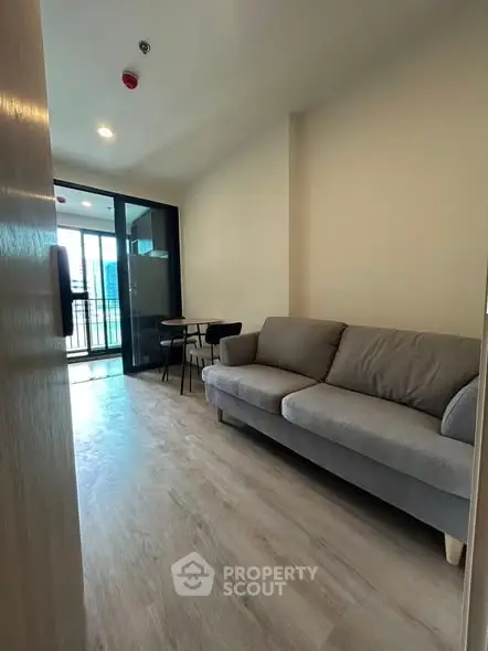 Modern living room with gray sofa and balcony view in urban apartment.