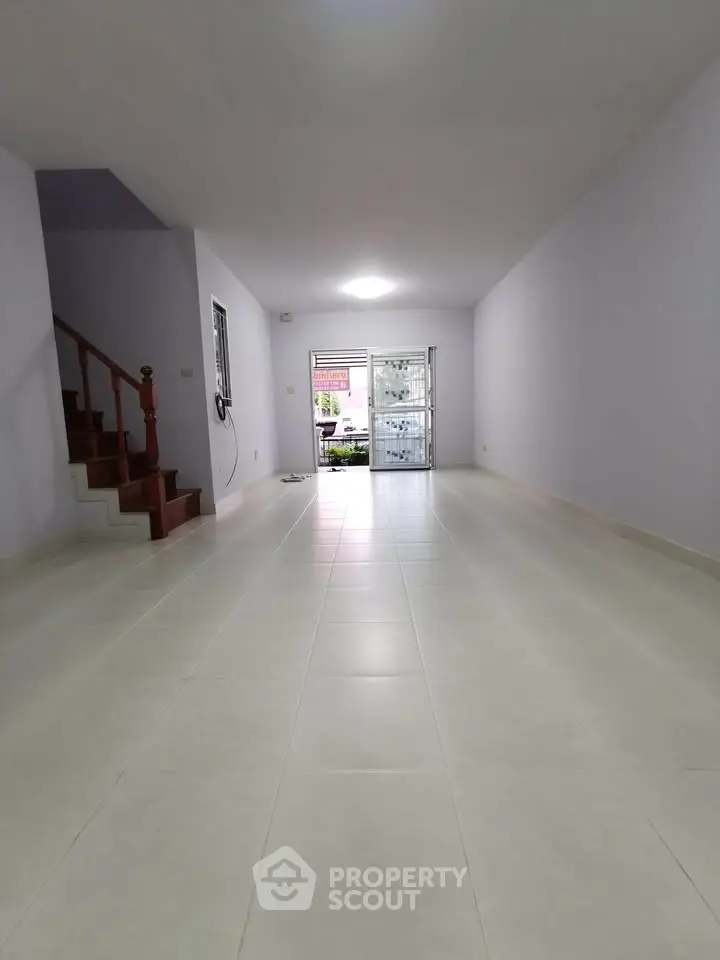 Spacious empty living room with tiled flooring and staircase, ideal for customization.