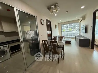 Modern apartment interior with open layout, featuring kitchen, dining area, and living room with balcony view.