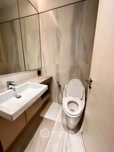 Modern bathroom with sleek fixtures and elegant marble walls, featuring a contemporary toilet and stylish sink.