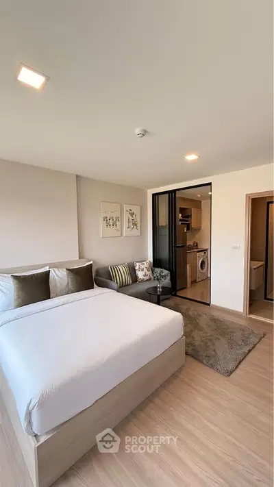 Modern studio apartment with cozy bed, stylish sofa, and compact kitchen featuring a washing machine.
