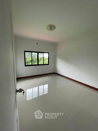 Spacious empty room with glossy tiled floor and large window offering natural light.