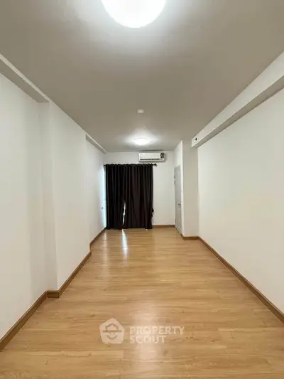 Spacious empty room with wooden flooring and large window, perfect for customization.