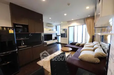 Modern living room with open kitchen, stylish decor, and large windows offering natural light.