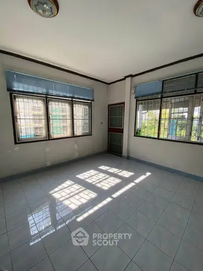 Spacious sunlit room with large windows and tiled flooring, perfect for versatile living space.