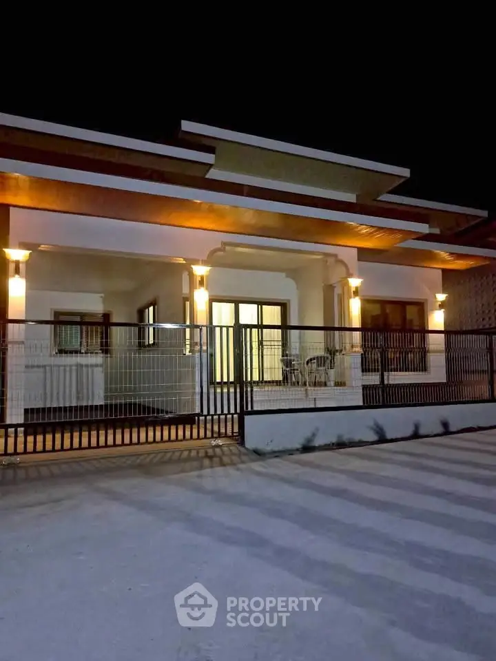Modern single-story house with illuminated facade and gated entrance at night.