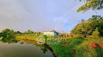 Charming rural property with lush greenery and serene pond under a rainbow sky.