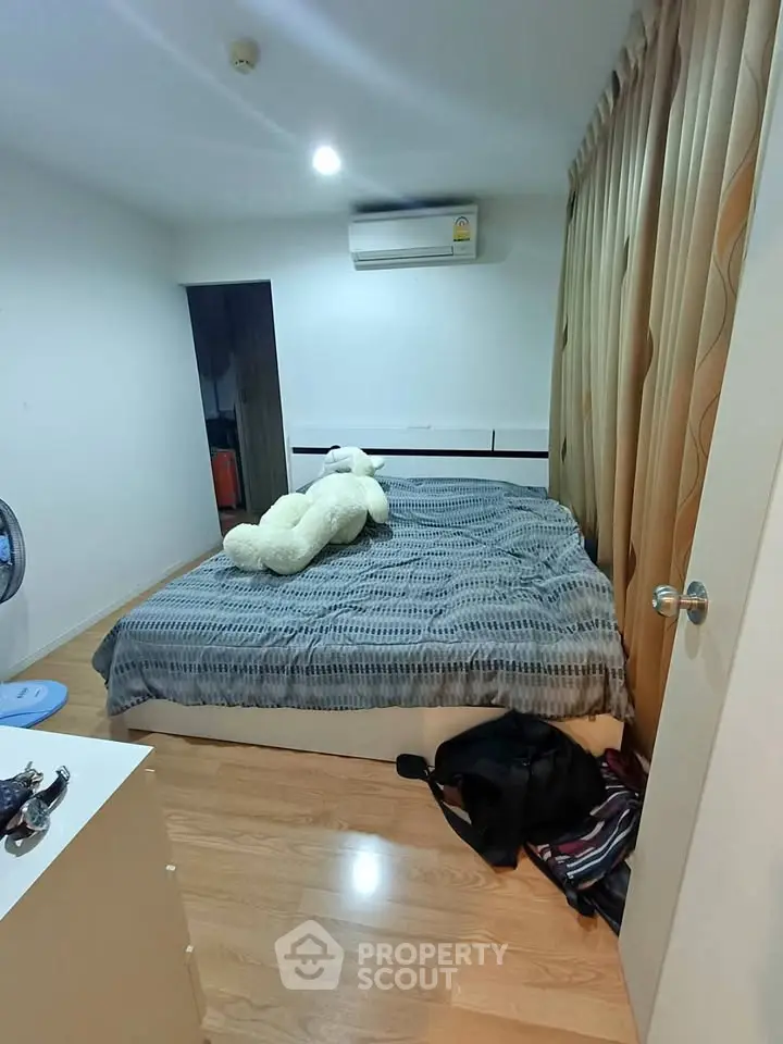 Cozy bedroom with wooden flooring and plush teddy bear on bed, featuring air conditioning and ample natural light.
