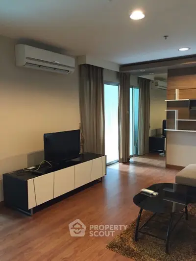 Modern living room with sleek furniture and wooden flooring, featuring a TV and air conditioning.