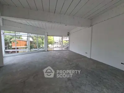 Spacious open-plan room with large windows and concrete flooring, ideal for versatile use.