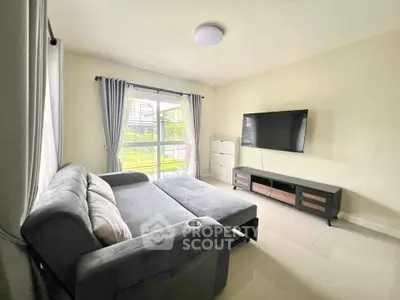 Spacious living room with modern sofa and large TV, featuring natural light from wide windows.