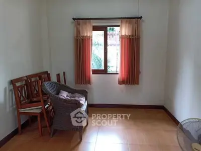 Cozy room with wicker chair and wooden chairs, featuring a window with curtains.