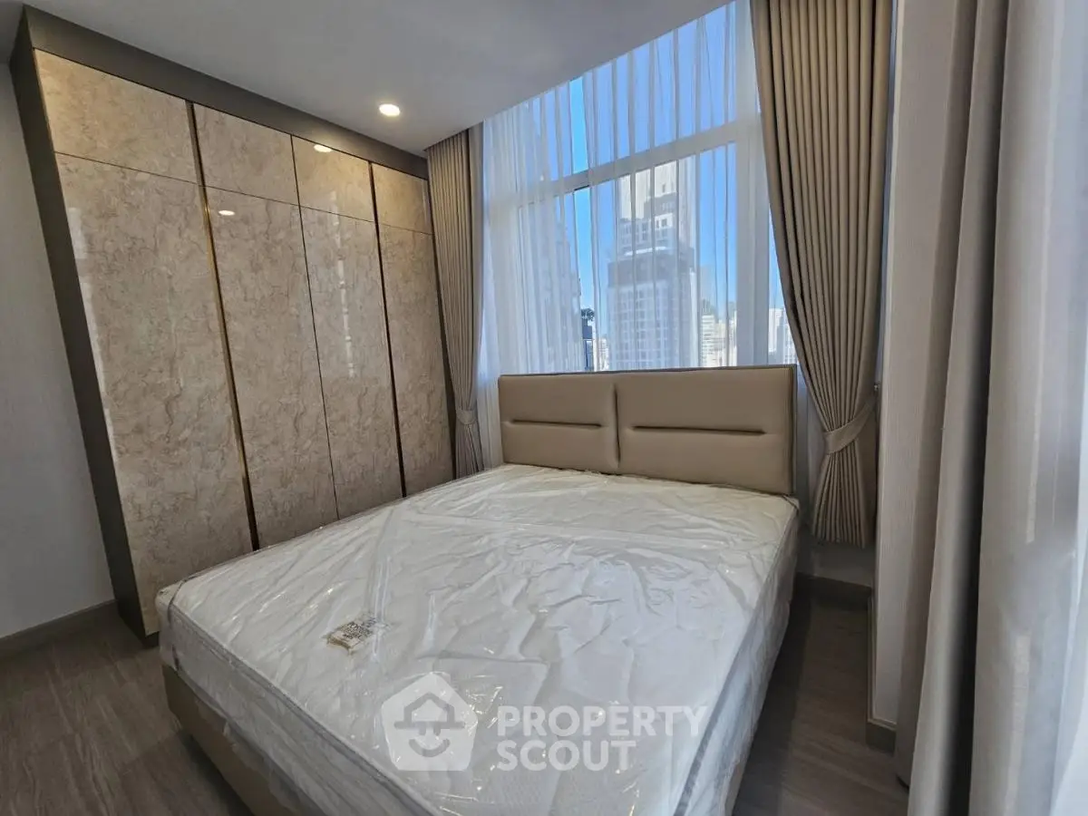 Modern bedroom with large window and city view, featuring a stylish bed and elegant curtains.