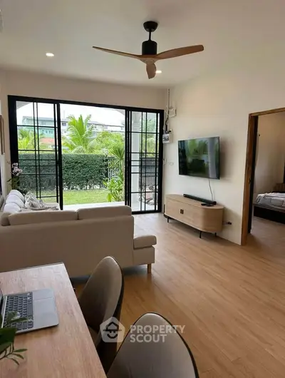 Modern living room with large windows and garden view, featuring stylish furniture and wooden flooring.