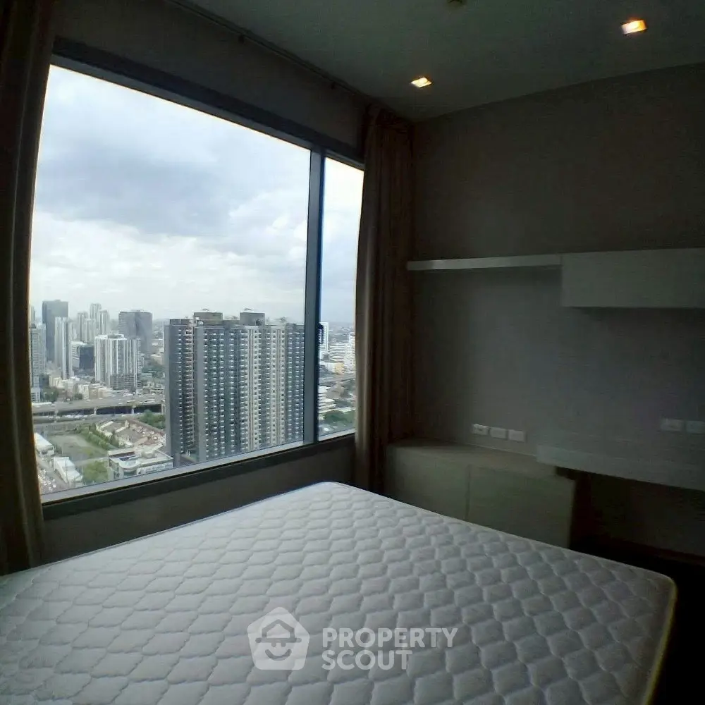 Modern bedroom with stunning city view from large window in high-rise apartment.