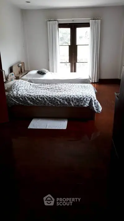 Cozy bedroom with twin beds and wooden flooring, featuring a large window for natural light.