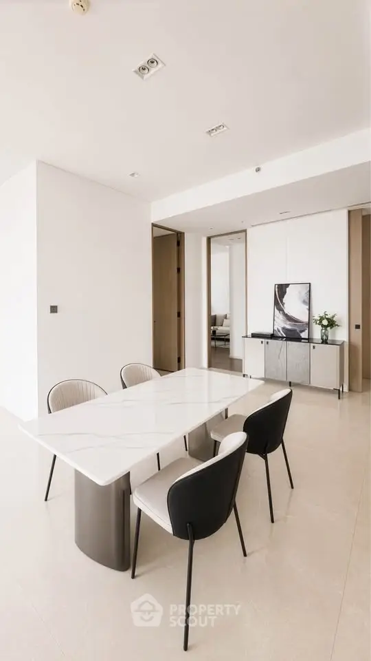 Modern dining area with sleek marble table and stylish chairs in a minimalist apartment.