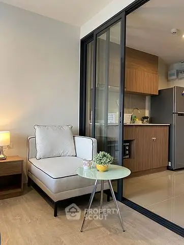 Modern living room with cozy chair and open kitchen layout, featuring sleek design and natural lighting.