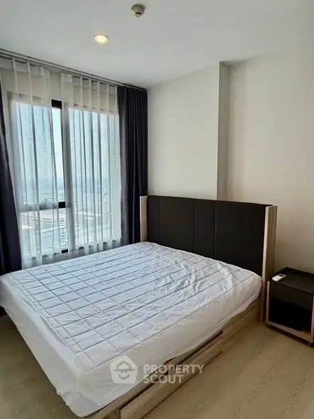 Modern bedroom with large window and stylish furnishings in a high-rise apartment.