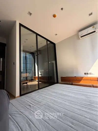 Modern bedroom with glass partition and air conditioning, featuring sleek design and natural light.