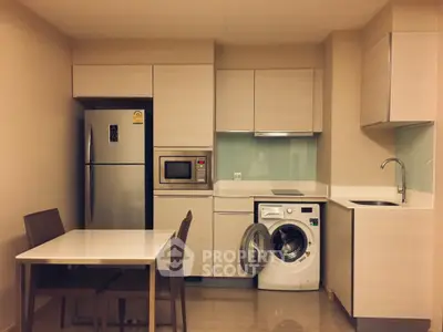 Modern kitchen with sleek cabinetry, dining area, and built-in appliances including washing machine and fridge.