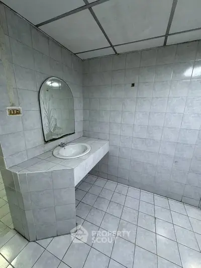 Spacious tiled bathroom with modern sink and mirror, ideal for renovation.