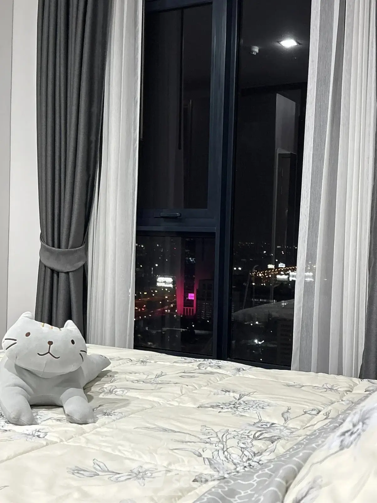 Cozy bedroom with city view, featuring plush bedding and elegant curtains for a serene ambiance.