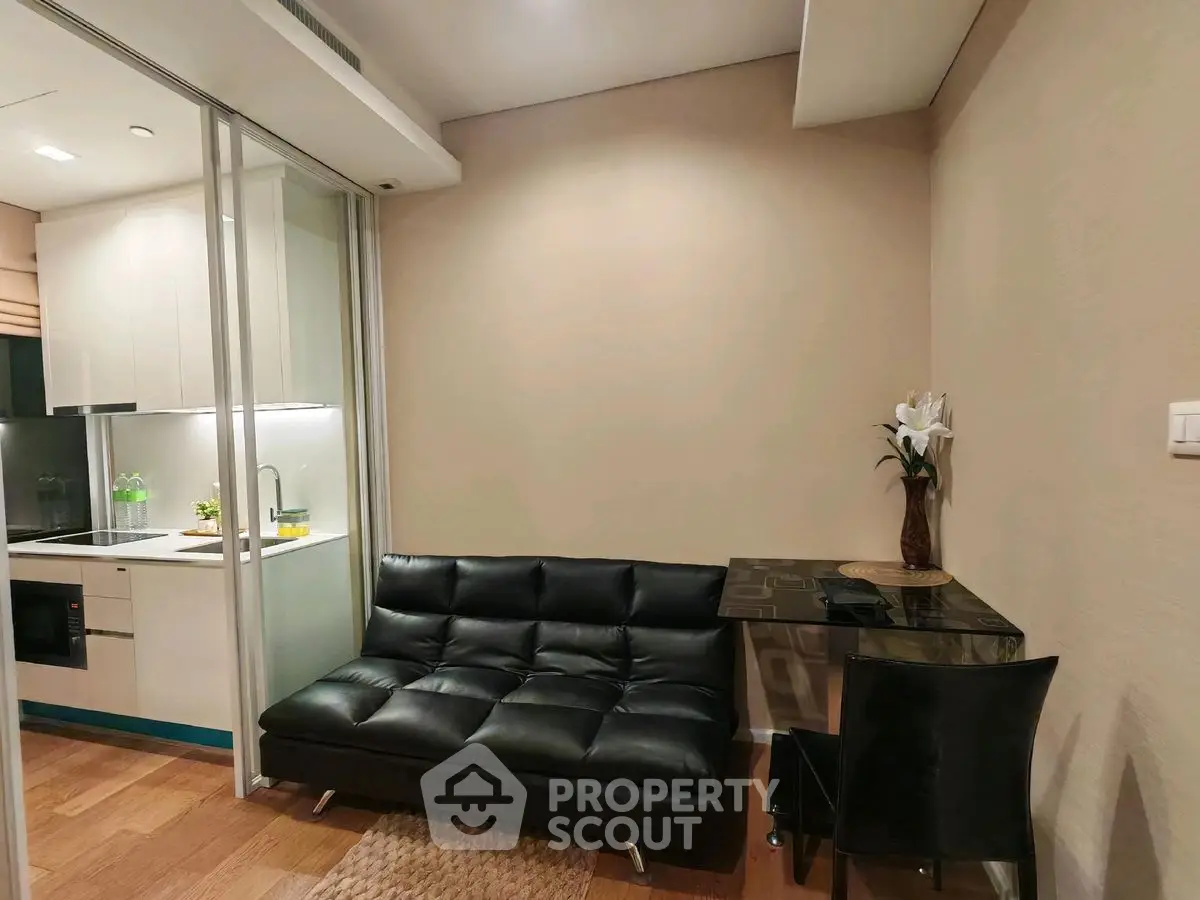 Modern compact living room with sleek black sofa and adjacent kitchen area
