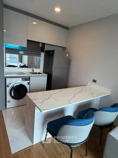 Modern kitchen with sleek marble island and built-in washing machine in stylish apartment.