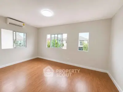 Spacious empty room with wooden flooring and large windows offering natural light.