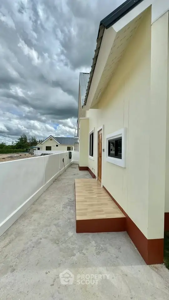 Modern exterior of a single-story home with a small wooden porch and cloudy sky.