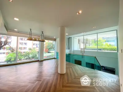 Spacious and modern living room with large windows offering ample natural light, sleek hardwood flooring, and a unique column design.