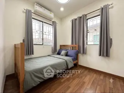 Cozy bedroom with wooden flooring and natural light, featuring a single bed and air conditioning.