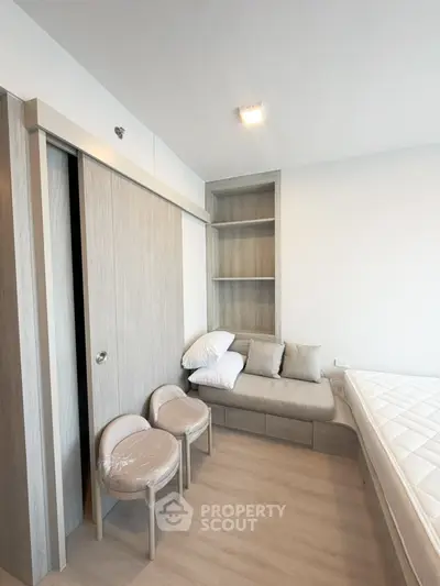 Modern bedroom with minimalist design, featuring built-in storage and cozy seating area.