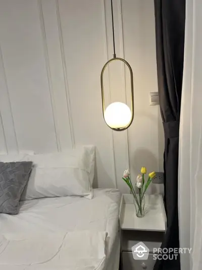 Cozy bedroom with modern pendant light and elegant white bedding, featuring a stylish nightstand with decorative flowers.